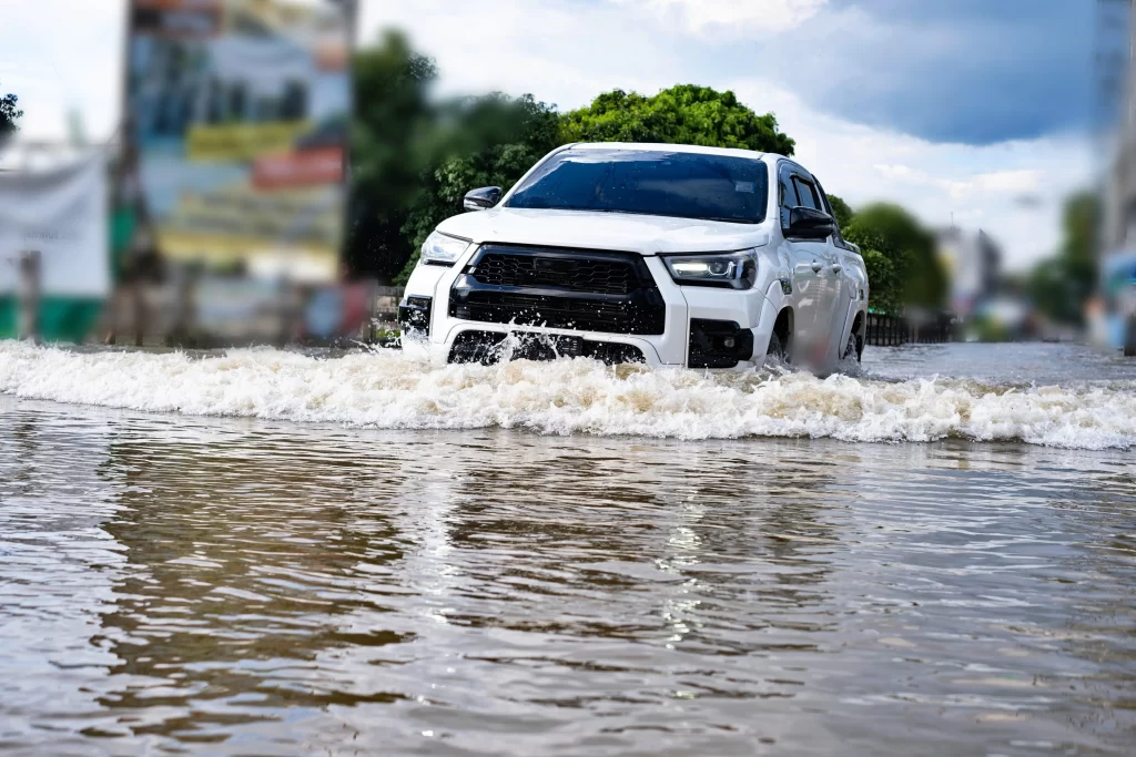 Auto projíždějící rozvodněnou silnicí. 