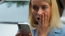 Žena udiveně hledí do mobilu.