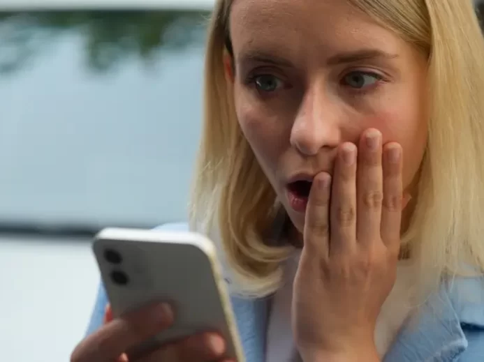 Žena udiveně hledí do mobilu.