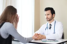 Doktor drží ženu za ruce na znamení podpory.