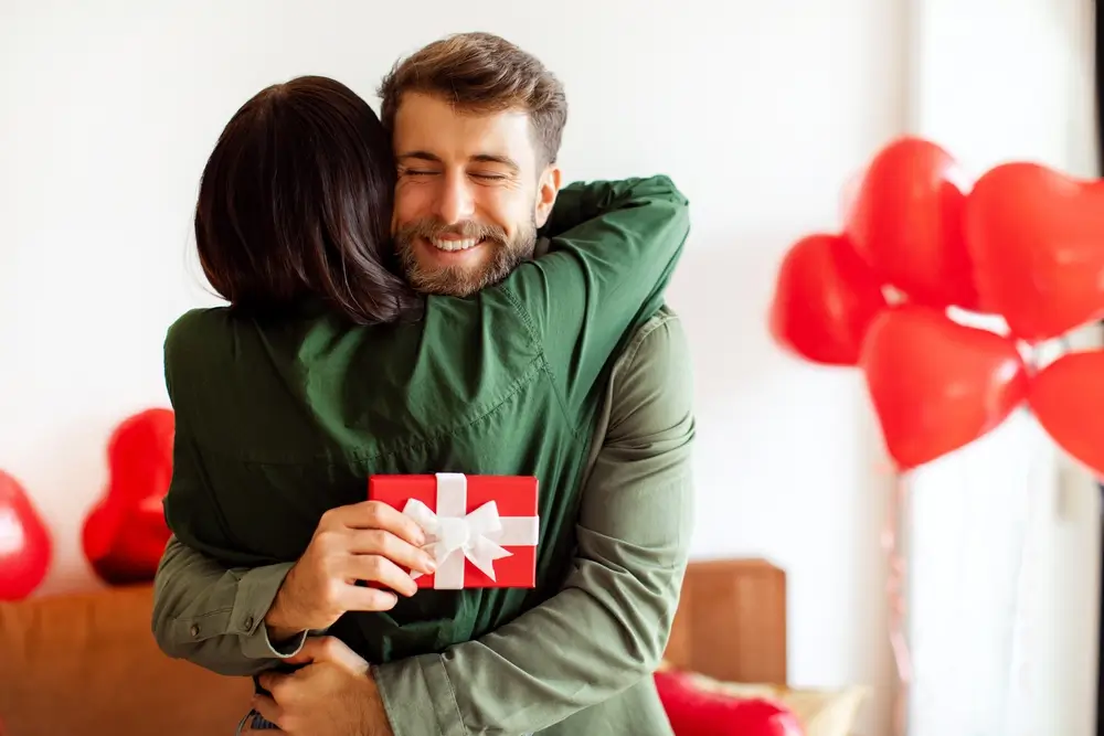 shutterstock_2567016649 - Pravda24 Muž se objímá se ženou a drží v ruce dárek.