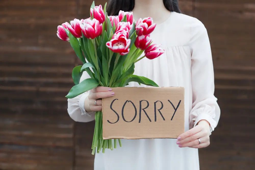 shutterstock_367740983 - Pravda24 Žena drží v ruce květiny a ceduli s nápisem „sorry".