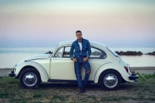Mladý muž se opírá o bílý Volkswagen brouk.