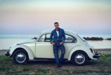 Mladý muž se opírá o bílý Volkswagen brouk.