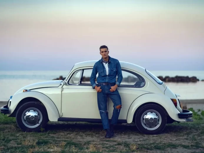 Mladý muž se opírá o bílý Volkswagen brouk.