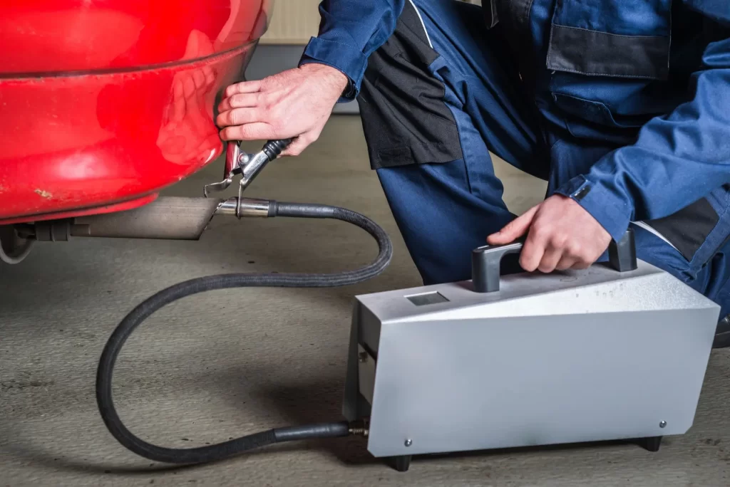 - Pravda24 Technik provádí měření emisí u výfuku červeného automobilu.