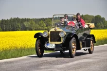 Historický vůz Laurin & Klement se třemi osobami projíždí krajinou