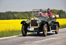 Historický vůz Laurin & Klement se třemi osobami projíždí krajinou