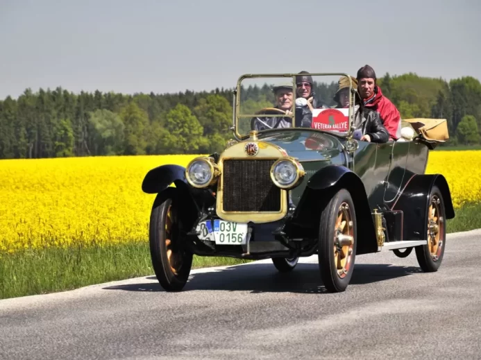 Historický vůz Laurin & Klement se třemi osobami projíždí krajinou
