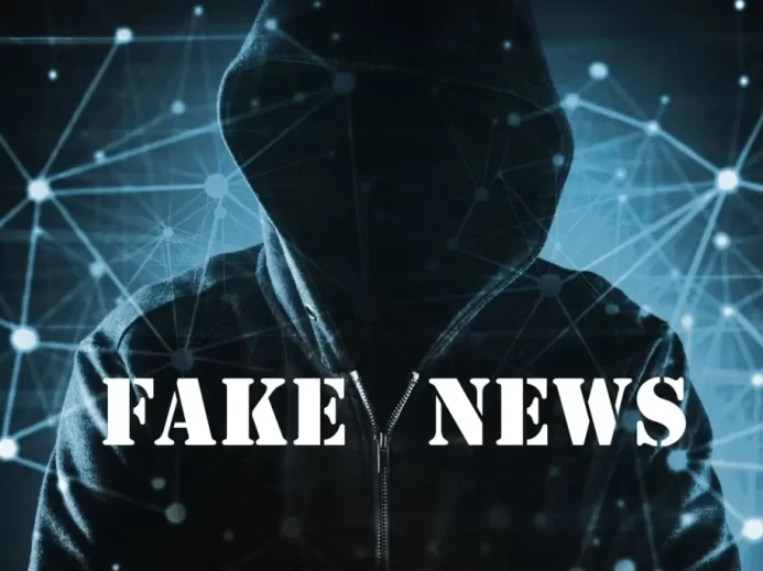 Temná postava v kapuci na pozadí digitální sítě s nápisem "Fake News"
