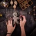 Ruce držící ručně vyrobenou voodoo panenku s jehlami, obklopenou přírodními artefakty, sušenými květy a dřevěnými nástroji při rituálu