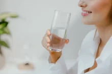Usměvavá žena v bílé košili drží v ruce sklenici čisté vody