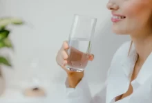 Usměvavá žena v bílé košili drží v ruce sklenici čisté vody
