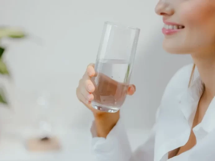 Usměvavá žena v bílé košili drží v ruce sklenici čisté vody