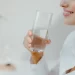 Usměvavá žena v bílé košili drží v ruce sklenici čisté vody