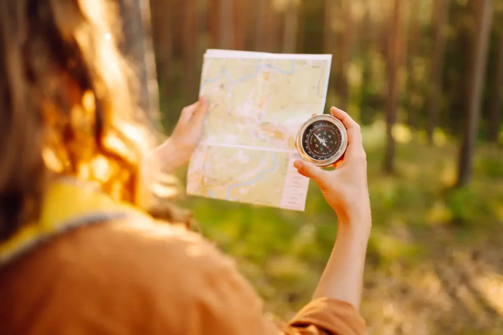 - Pravda24 Žena v lese držící papírovou mapu a klasický kompas v ruce během turistické výpravy