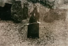 Ženy v dlouhém černém plášti a špičatém klobouku, držící koště
