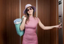 Žena v růžových šatech, klobouku a slunečních brýlích mačká tlačítko výtahu