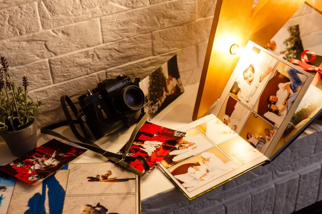 - Pravda24 Starý fotoaparát vedle otevřené fotoknihy plné rodinných snímků položený na stole pod lampou