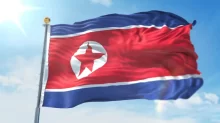 Vlající státní vlajka Severní Koreje s červenou hvězdou a modrými pruhy proti modré obloze