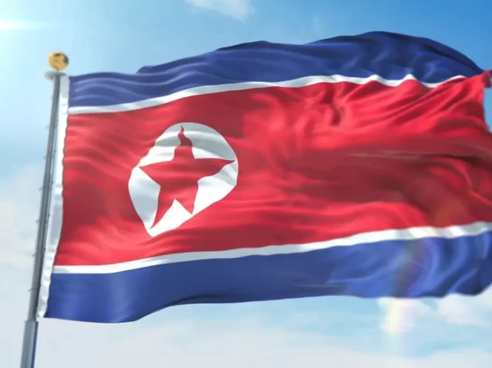 Vlající státní vlajka Severní Koreje s červenou hvězdou a modrými pruhy proti modré obloze