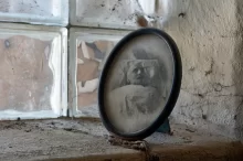 Zašlá oválná fotografie muže na smrtelné posteli, postavená na zaprášeném parapetu