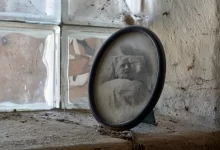 Zašlá oválná fotografie muže na smrtelné posteli, postavená na zaprášeném parapetu