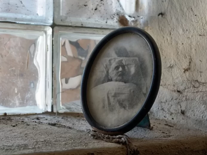 Zašlá oválná fotografie muže na smrtelné posteli, postavená na zaprášeném parapetu