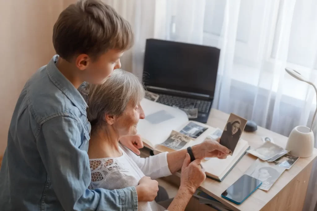 - Pravda24 Starší žena s vnukem si prohlížejí černobílé rodinné fotografie u stolu s albem a notebookem