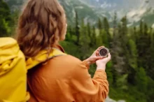 Turistka s batohem drží kompas při cestě přírodou