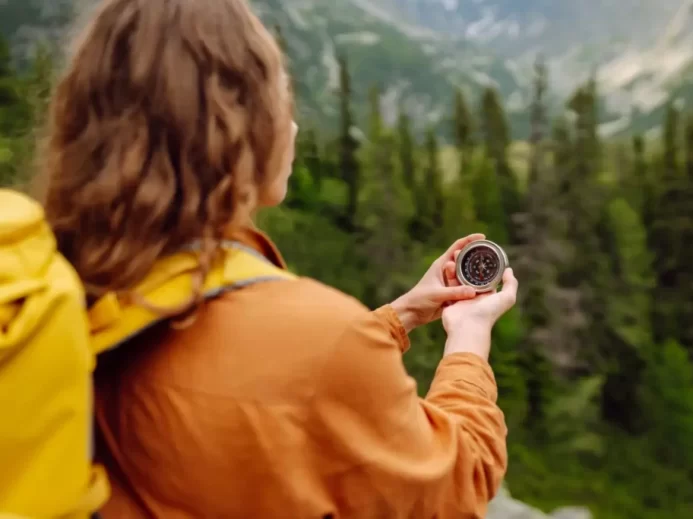 Turistka s batohem drží kompas při cestě přírodou
