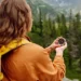 Turistka s batohem drží kompas při cestě přírodou