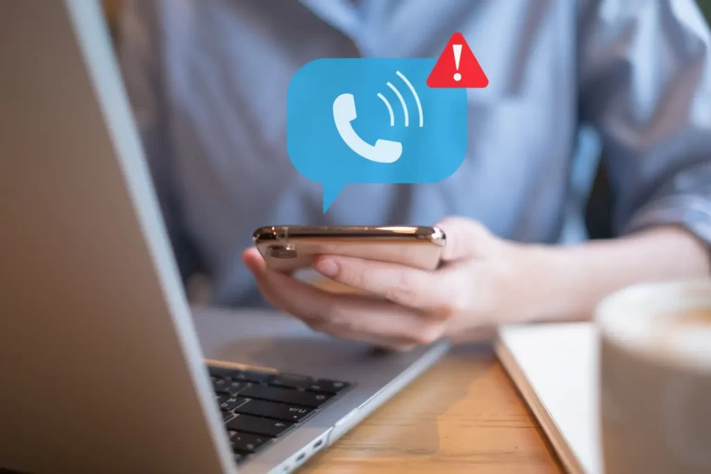 - Pravda24 Osoba drží smartphone s ikonou varovného hovoru, v pozadí je laptop a káva