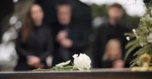 bílá růže na rakvi a pozůstalí v pozadí