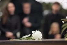 bílá růže na rakvi a pozůstalí v pozadí