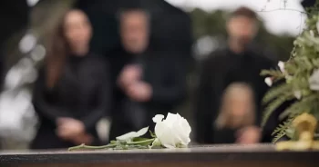 bílá růže na rakvi a pozůstalí v pozadí