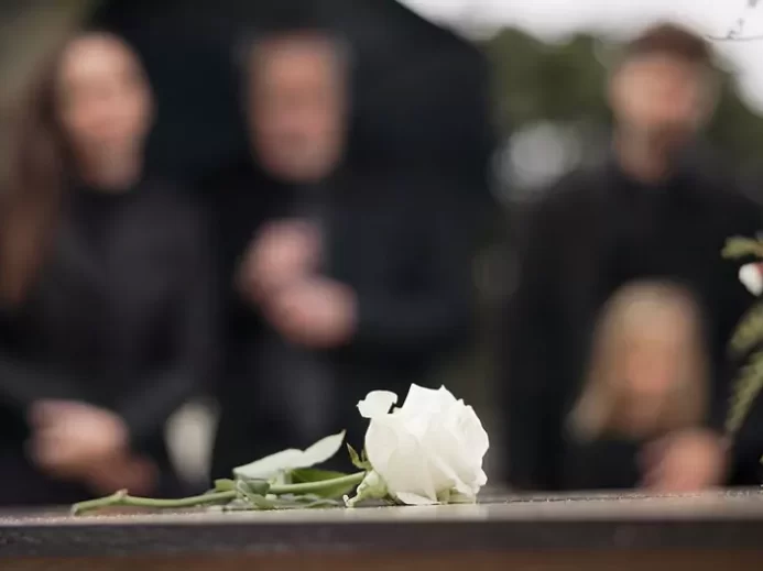 bílá růže na rakvi a pozůstalí v pozadí