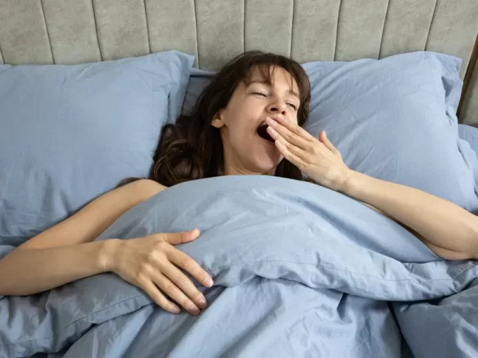 Zívající žena ležící v posteli