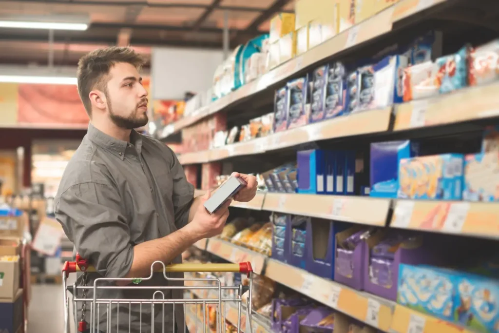 - Pravda24 Muž se zastavil u regálu v supermarketu a zkoumá obal výrobku, zatímco má u sebe nákupní vozík