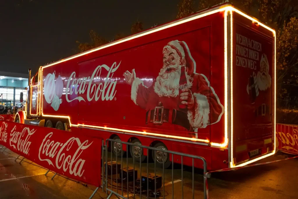 Červený kamion Coca Coly s vyobrazením Santa Clause a vánočními světly stojí připraven na večerní show v ulicích města