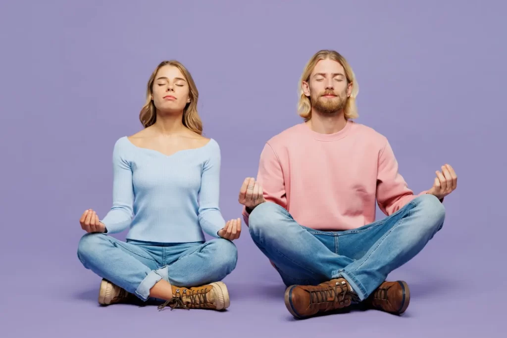 Žena v modrém svetru a muž v růžové mikině sedí v meditační pozici