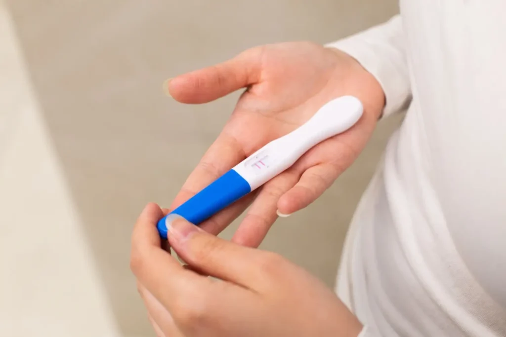 Detail ženy držící pozitivní těhotenský test s dvěma růžovými čárkami