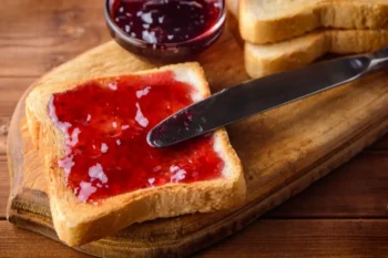 Plátek toastového chleba namazaný jahodovým džemem na dřevěném prkénku s nožem