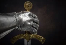 Detail kovové rukavice rytíře svírající meč se zdobenou zlatou rukojetí