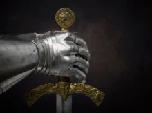 Detail kovové rukavice rytíře svírající meč se zdobenou zlatou rukojetí