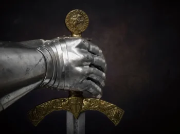 Detail kovové rukavice rytíře svírající meč se zdobenou zlatou rukojetí