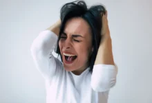 Žena v bílém triku křičí a drží se za hlavu, znázornění emočního vypětí spojovaného s hysterií