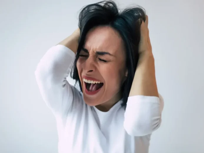 Žena v bílém triku křičí a drží se za hlavu, znázornění emočního vypětí spojovaného s hysterií