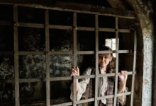 Žena ve starodávném oblečení zavřená za kovovou mříží v temné cele.